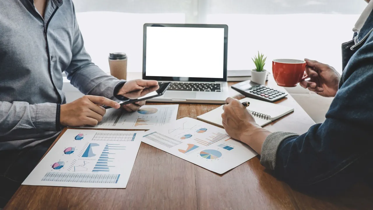 Duas pessoas analisando relatórios e gráficos em uma mesa de trabalho